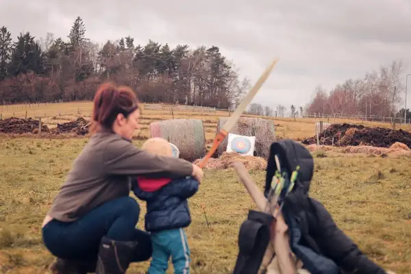 Maminka s dítětem střílí z luku na statku