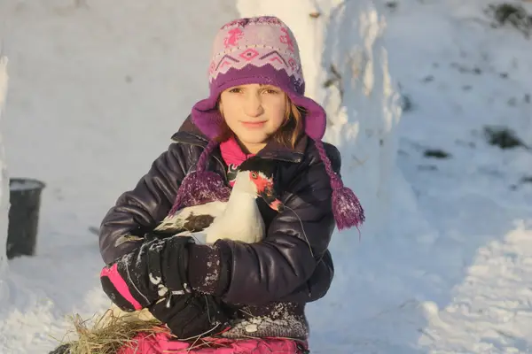 Dívka drží kachnu na zasněženém dvoře statku